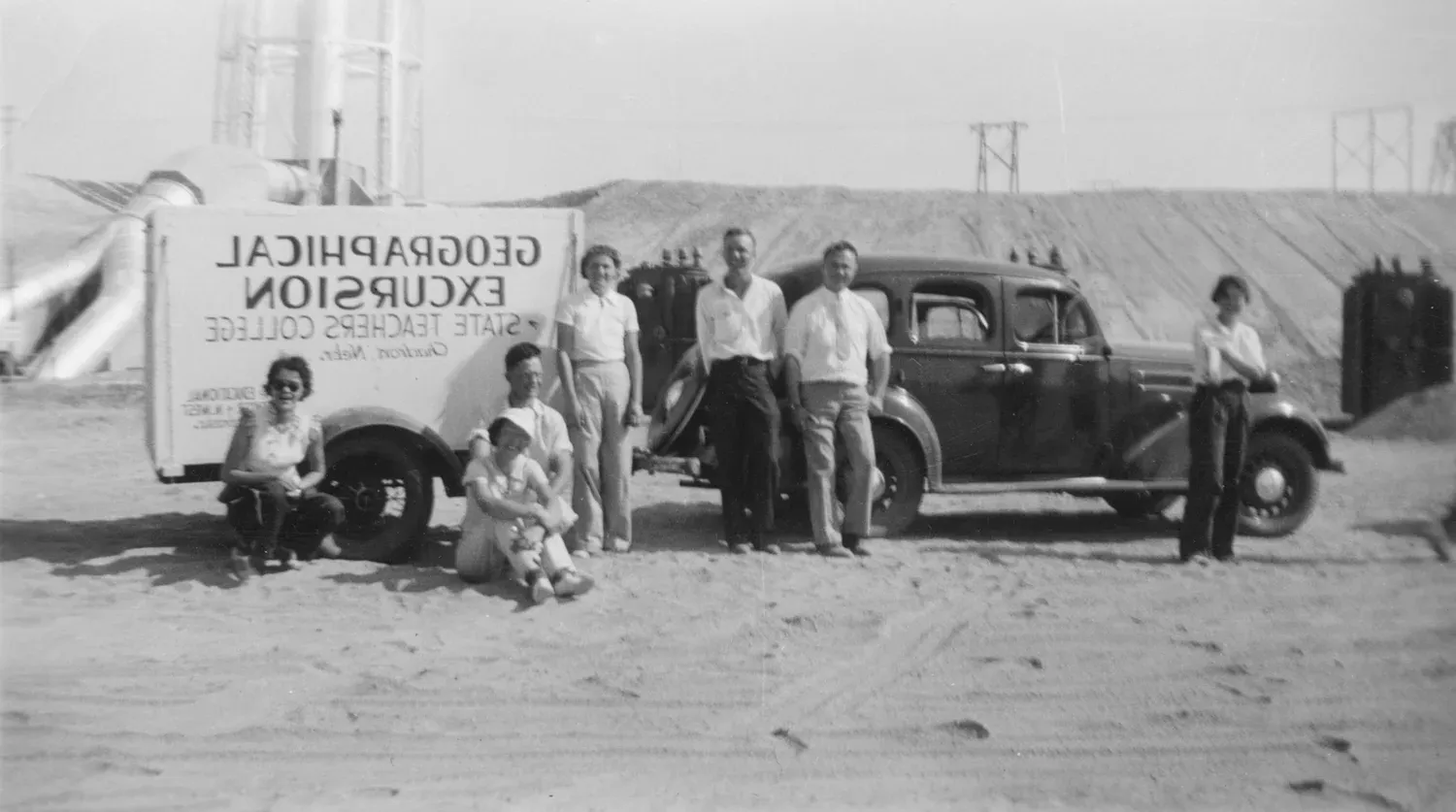 Group of people standing in front of a car with towed trailer