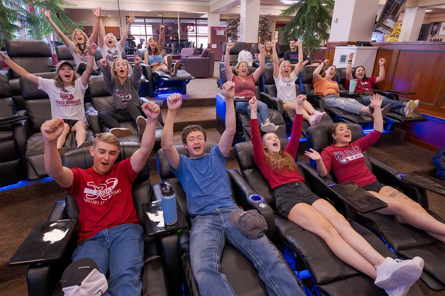 A large group of students cheer while watching TV